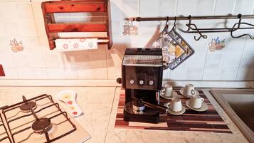 A kitchen with a gas stove, a coffee machine, and a hanging rack with pots.