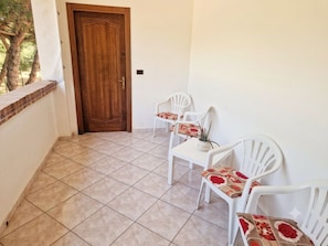 A balcony with a wooden door, white plastic chairs, and a tiled floor.