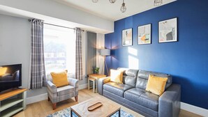 Un salon moderne avec un mur d’accent bleu, un canapé en cuir, une table basse en bois et un téléviseur.