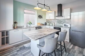 Een moderne keuken met een marmeren eiland, barstoelen en roestvrijstalen apparatuur.