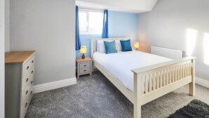 Une chambre à coucher avec un lit, des tables de chevet, une commode et une fenêtre avec des rideaux.