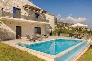 A two-story stone house with a swimming pool, outdoor seating, and a view of the hills. - Petradi Villa Skala III (Kefalonia)
