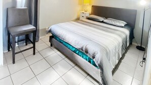 Et hotelværelse med en seng, en stol, et natbord, en lampe og en loftsvifte.