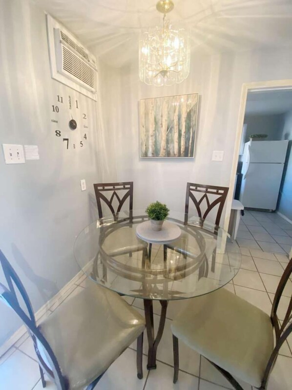 A dining area with a glass table and chairs, a chandelier, a wall clock, and a painting.