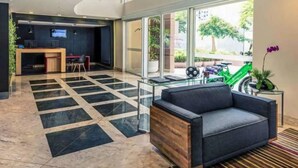 A modern lobby with a reception desk, seating area, and large windows offering a view of the outdoors. - Loft-In Jardins Ibirapuera X (Paraíso São Paulo)