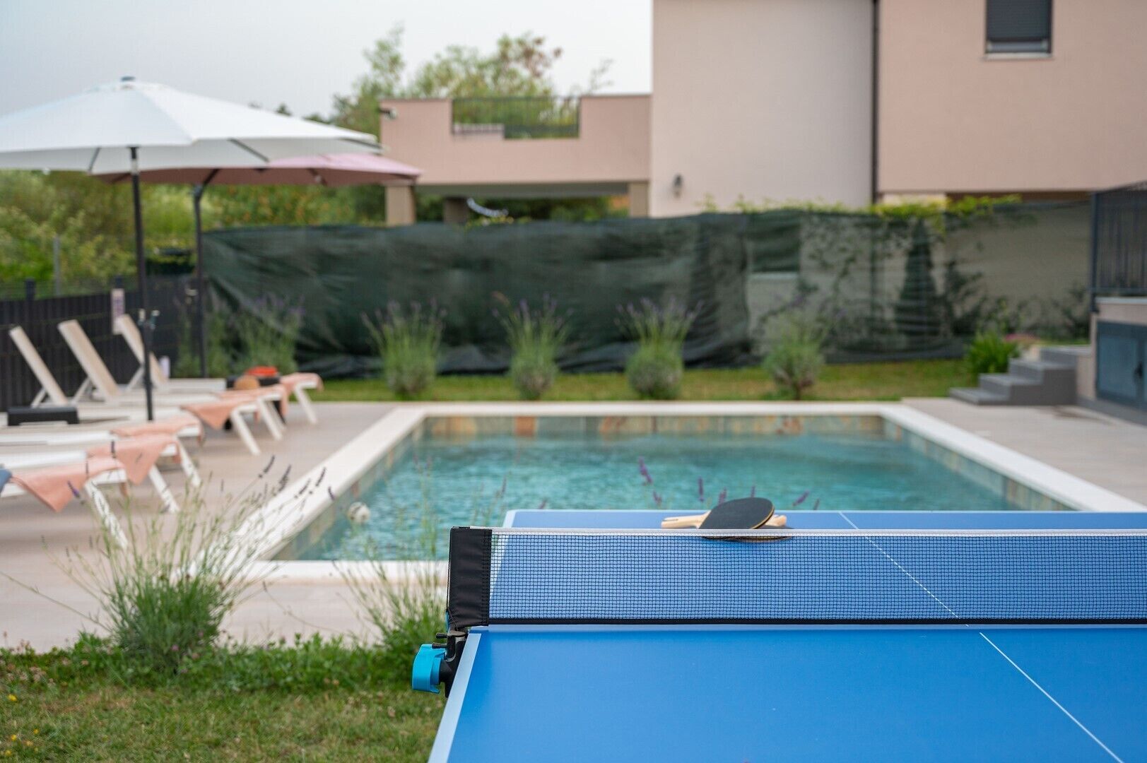 Ein Pool mit Liegestühlen und einem Tischtennis-Tisch in einem Garten.