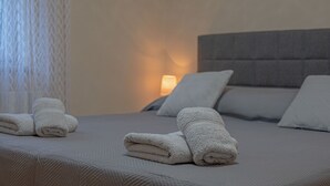 A neatly made bed with a grey headboard and pillows, a bedside lamp, and folded towels on the bed. - Poolside Holiday House (Labin)