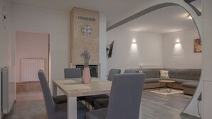 A modern living room with a grey sofa, a wooden dining table with chairs, and a fireplace. - Poolside Holiday House (Labin)