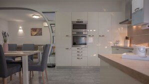 A modern kitchen with white cabinets, a built-in oven, and a dining area with a table and chairs. - Poolside Holiday House (Labin)
