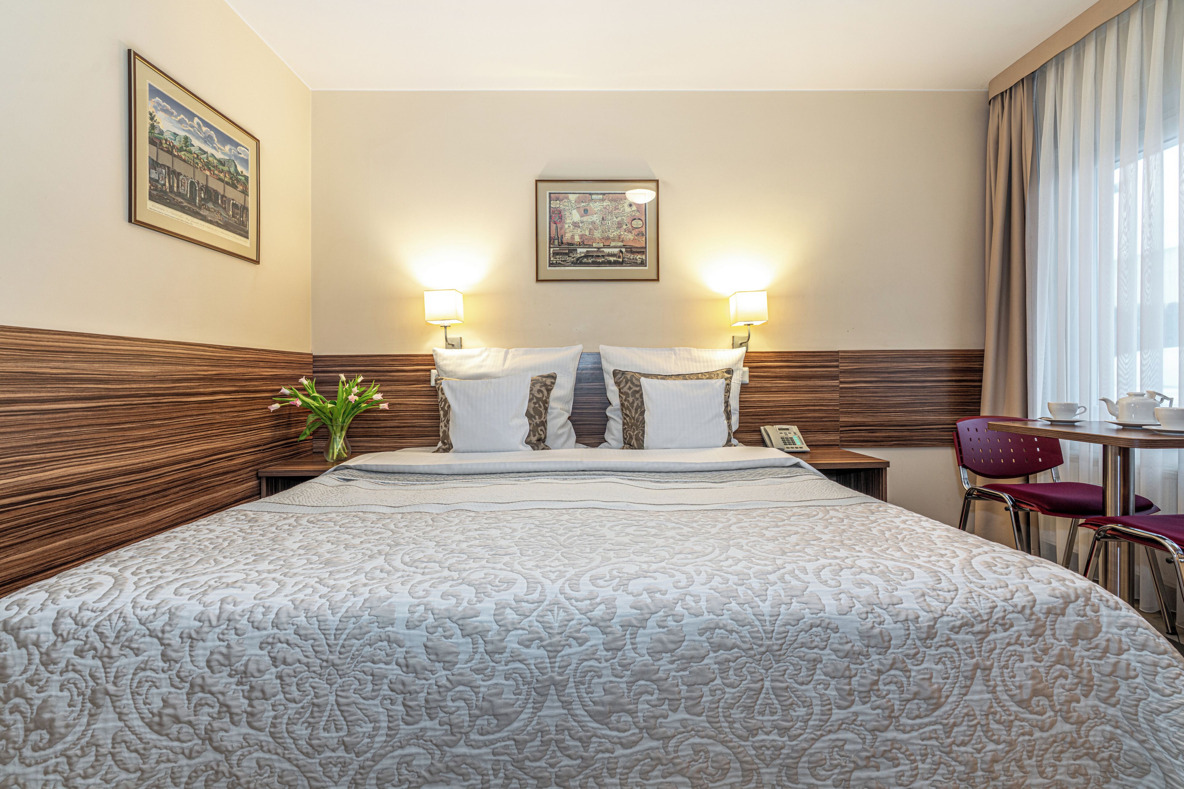 Ein Hotelzimmer mit einem großen Bett, zwei Nachttischlampen, einem gerahmten Bild an der Wand, einem kleinen Tisch mit Teekanne und einem Sessel.