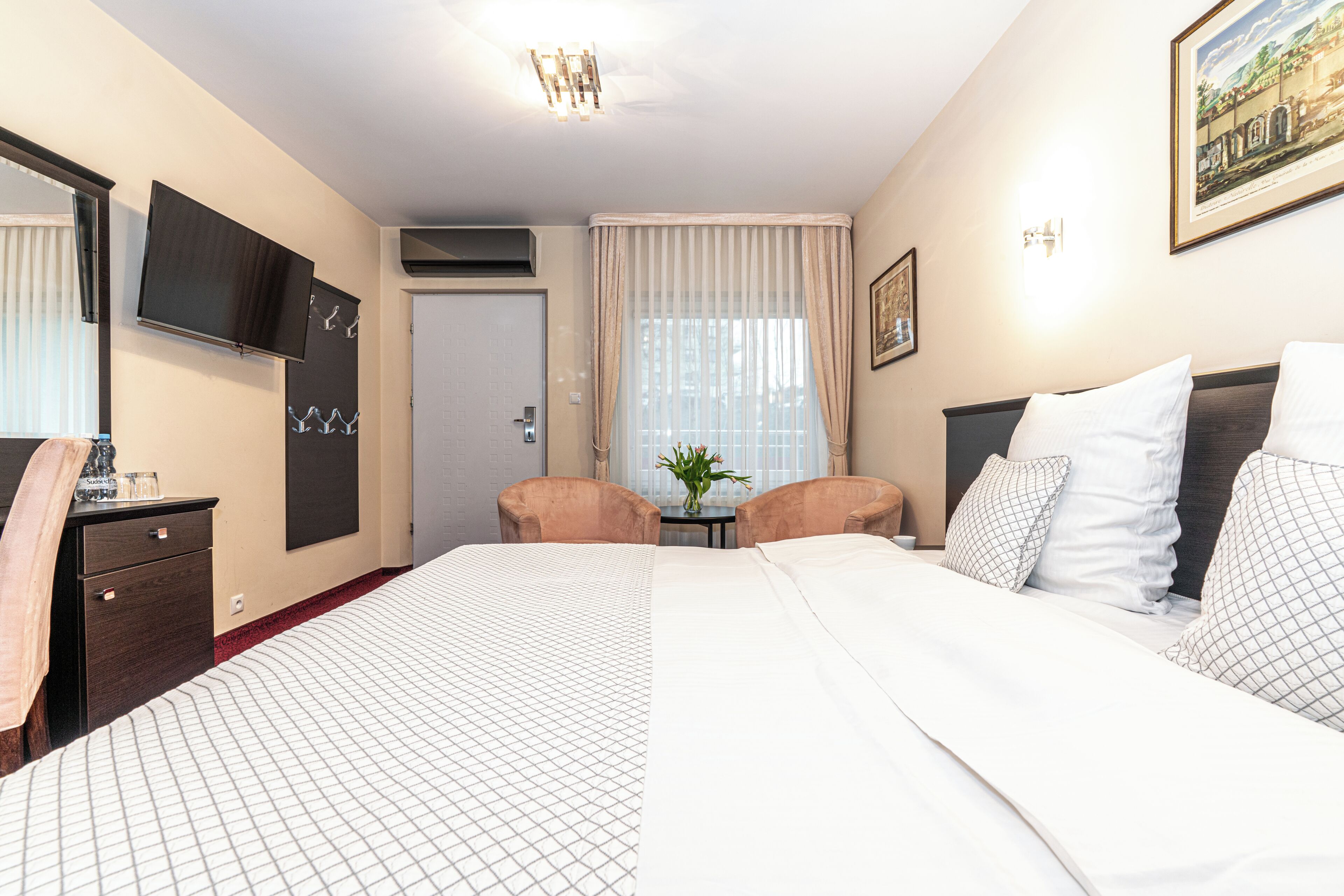 A hotel room with a large bed, a desk with a chair, a television, and a window with curtains.