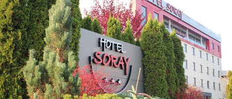 A hotel sign with the name 'Hotel Soray' surrounded by evergreen trees and red foliage.
