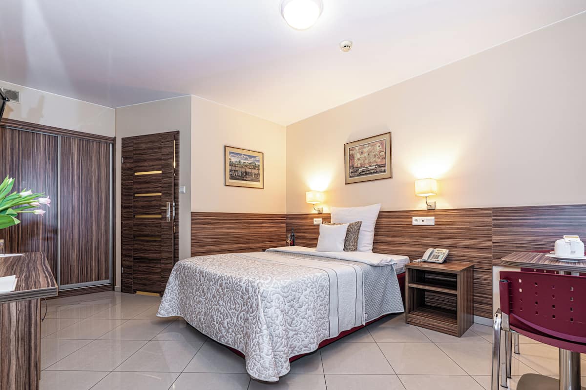 A hotel room with a bed, bedside lamps, a desk with a phone, and a chair.