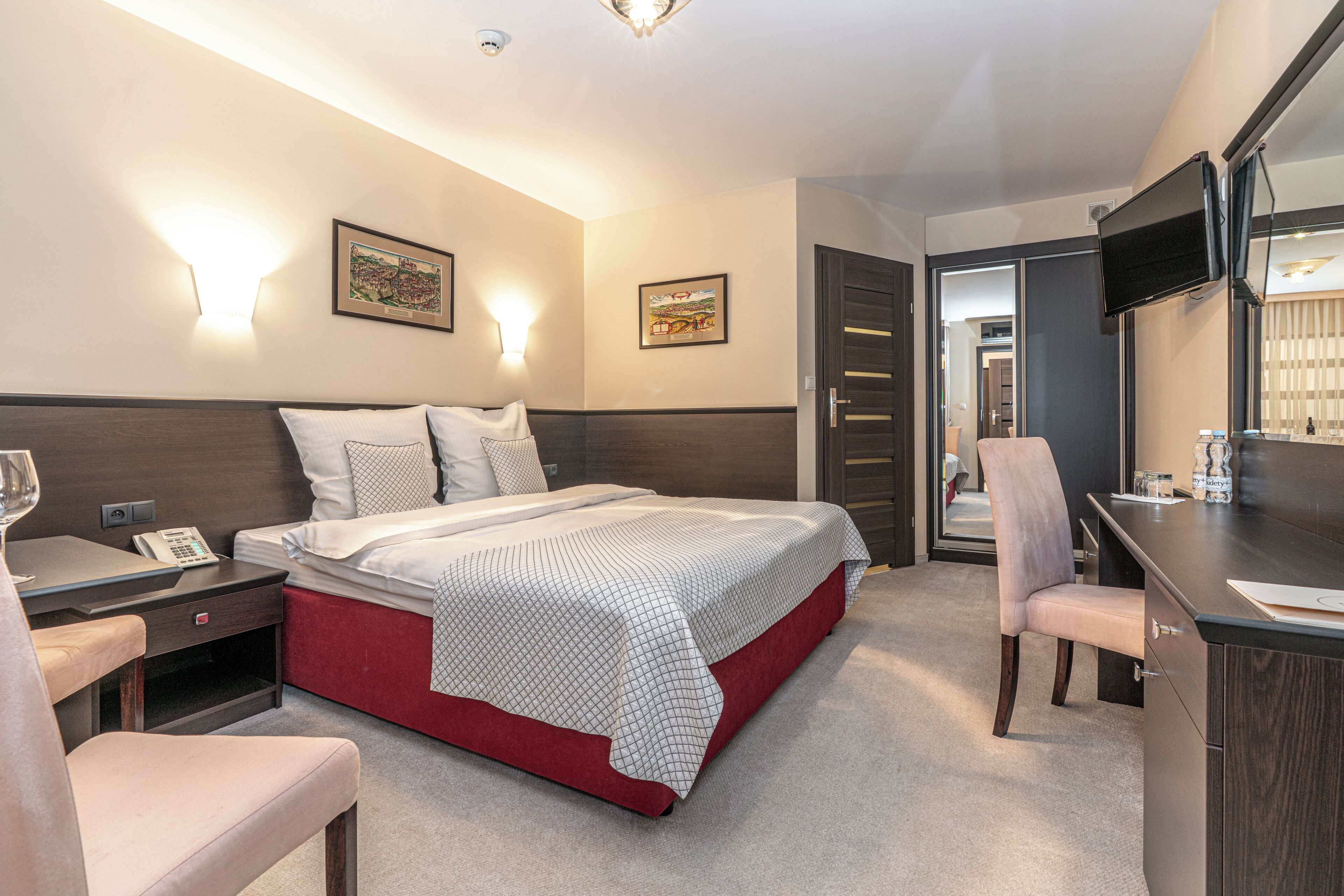 Habitación de hotel con cama, mesita de noche, silla, escritorio y televisión montada en la pared.