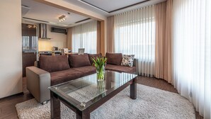 A modern living room with a glass coffee table, brown sofa, and a kitchen in the background. - Hotel Soray (Wieliczka)