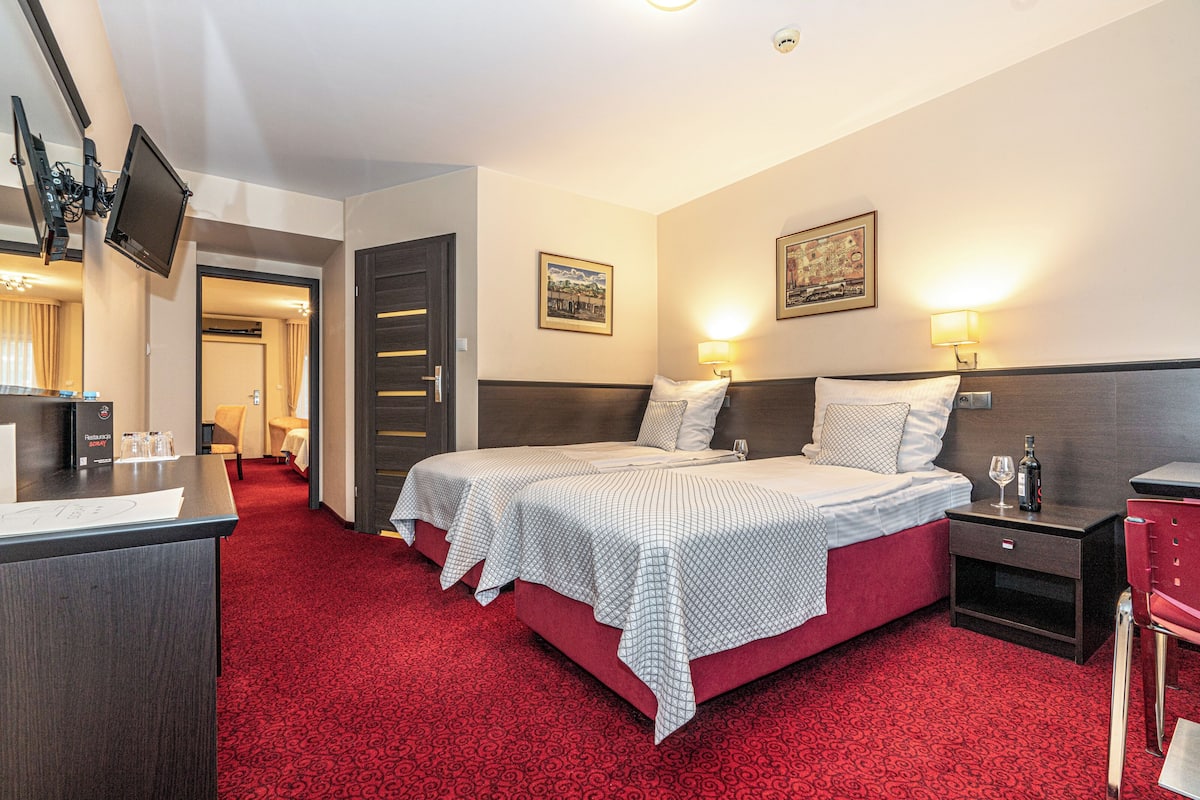 A hotel room with two beds, a desk, a chair, and a TV mounted on the wall.