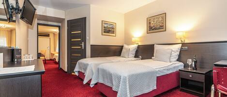 A hotel room with two beds, a desk, a chair, and a TV mounted on the wall.