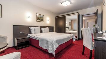 Quarto de hotel com cama, mesa de cabeceira, cadeira, escrivaninha e espelho.
