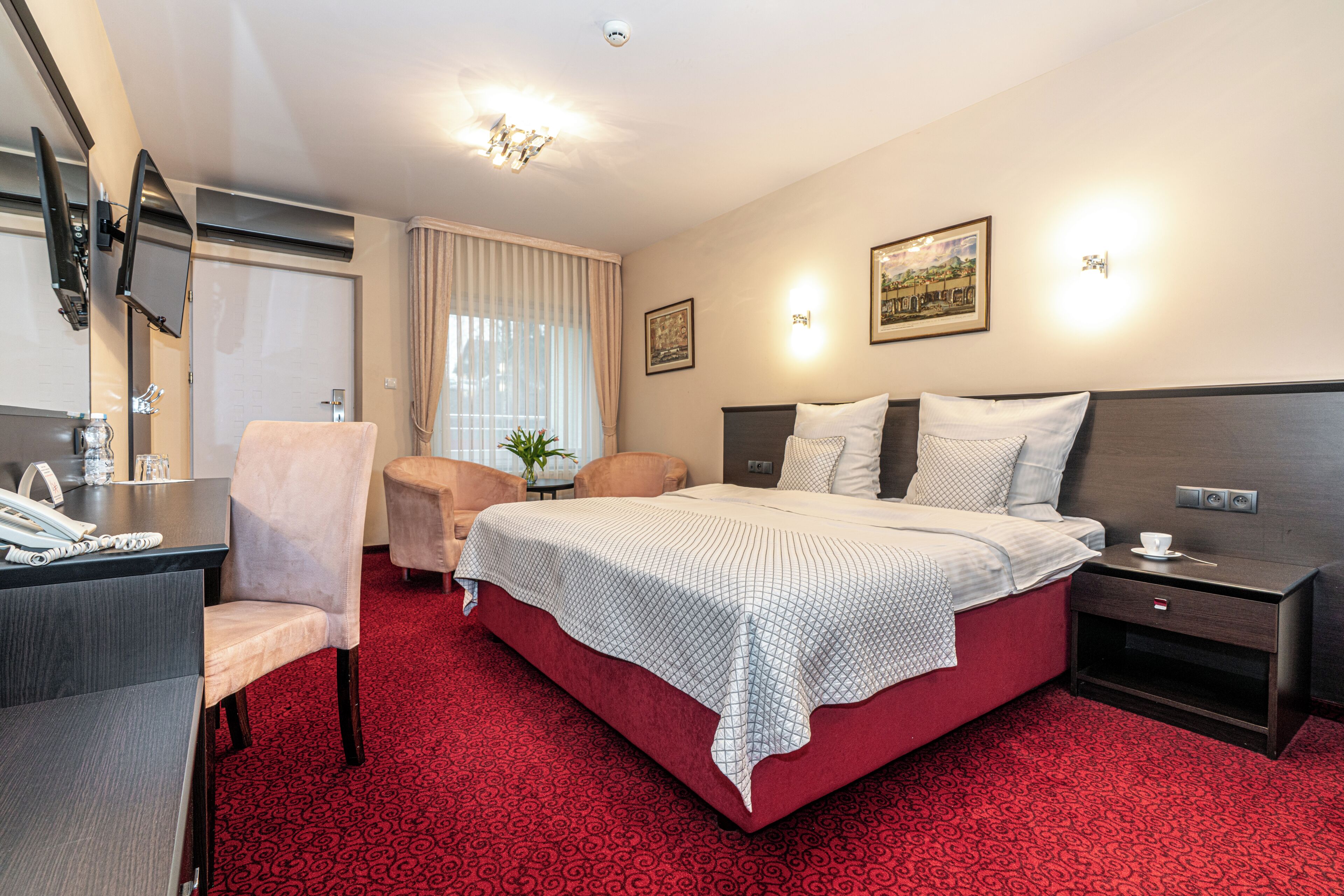 A hotel room with a bed, a desk, a chair, a TV, and a nightstand.