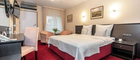 Una camera d'albergo con un letto, una scrivania, una sedia, una TV e un comodino.