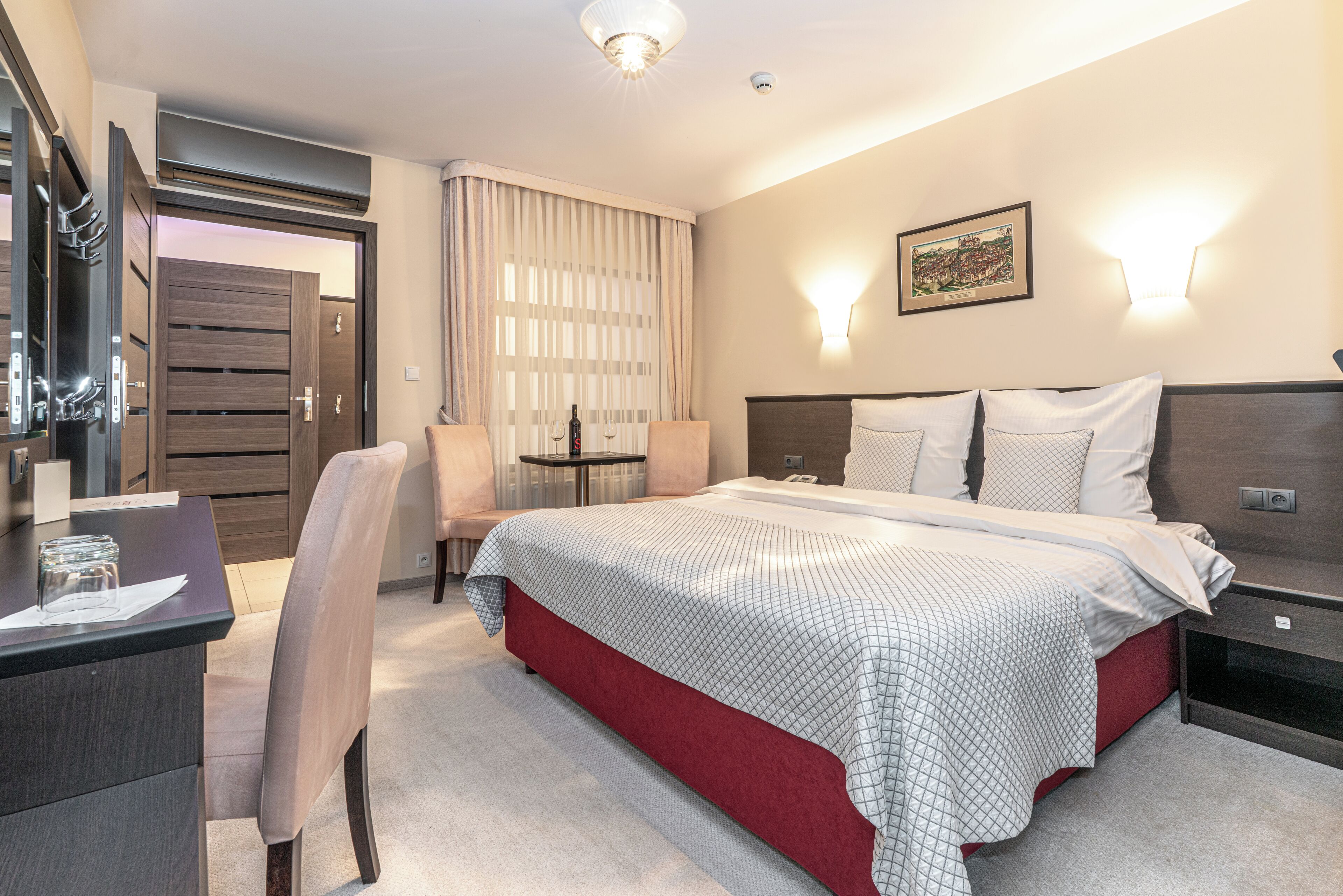 Una habitación de hotel con una cama, un escritorio, una silla, una mesa y una lámpara fijada a la pared.