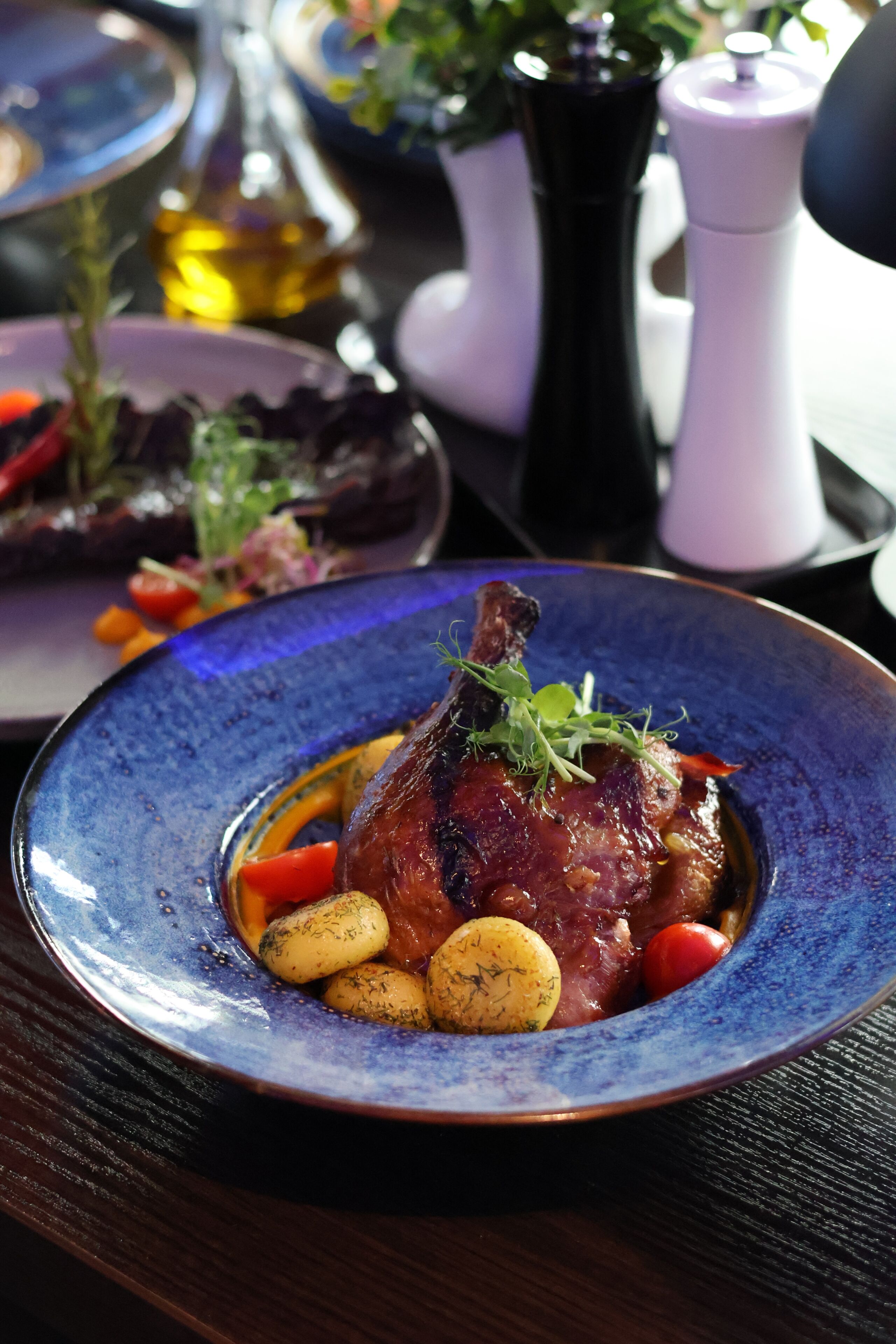 A plate of food with a lamb shank, potatoes, and vegetables.