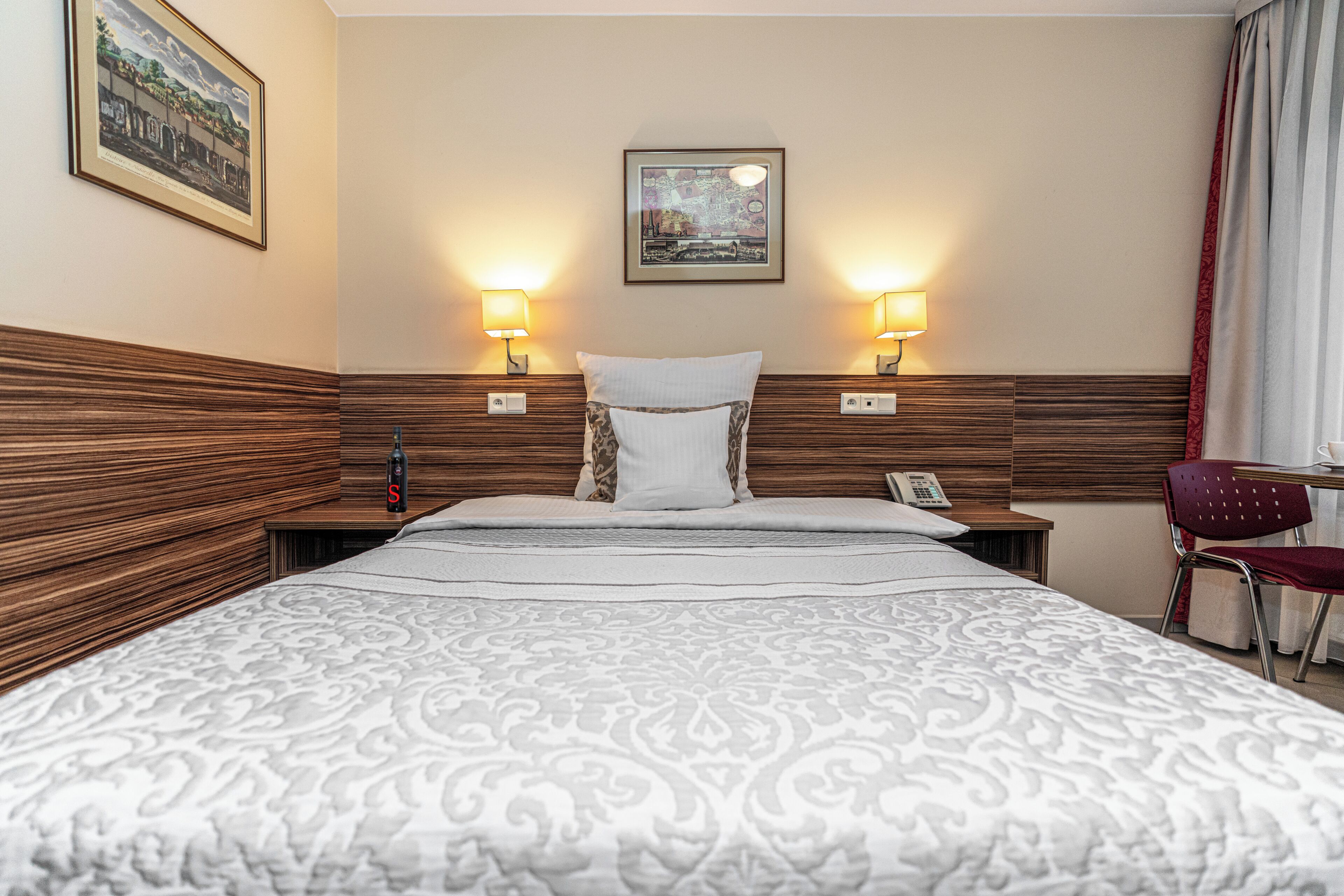 Habitación de hotel con una cama grande, dos lámparas de noche, un teléfono, una silla y un cuadro en la pared.