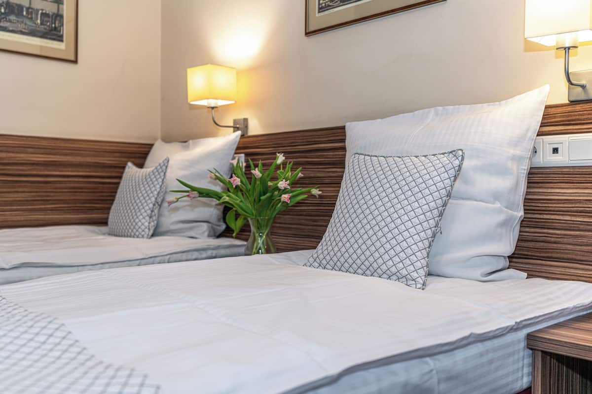 A hotel room with two beds, a wooden headboard, bedside lamps, a vase with flowers, and a framed picture on the wall.