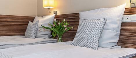 Een hotelkamer met twee bedden, een houten hoofdeinde, bedlampjes, een vaas met bloemen en een ingelijst foto aan de muur.