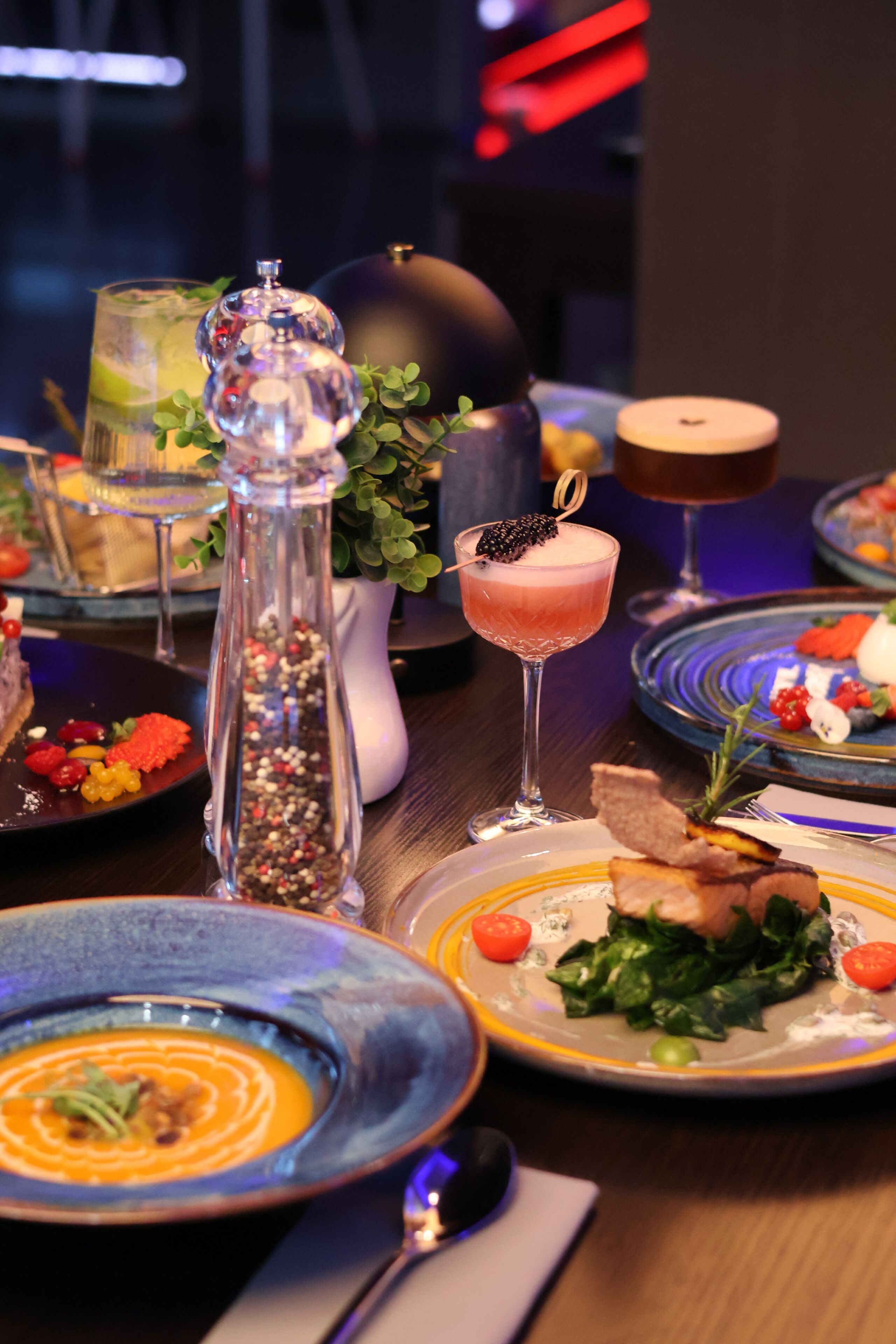 Una mesa de comedor con varios platos, entre ellos una ensalada, sopa y un cóctel.