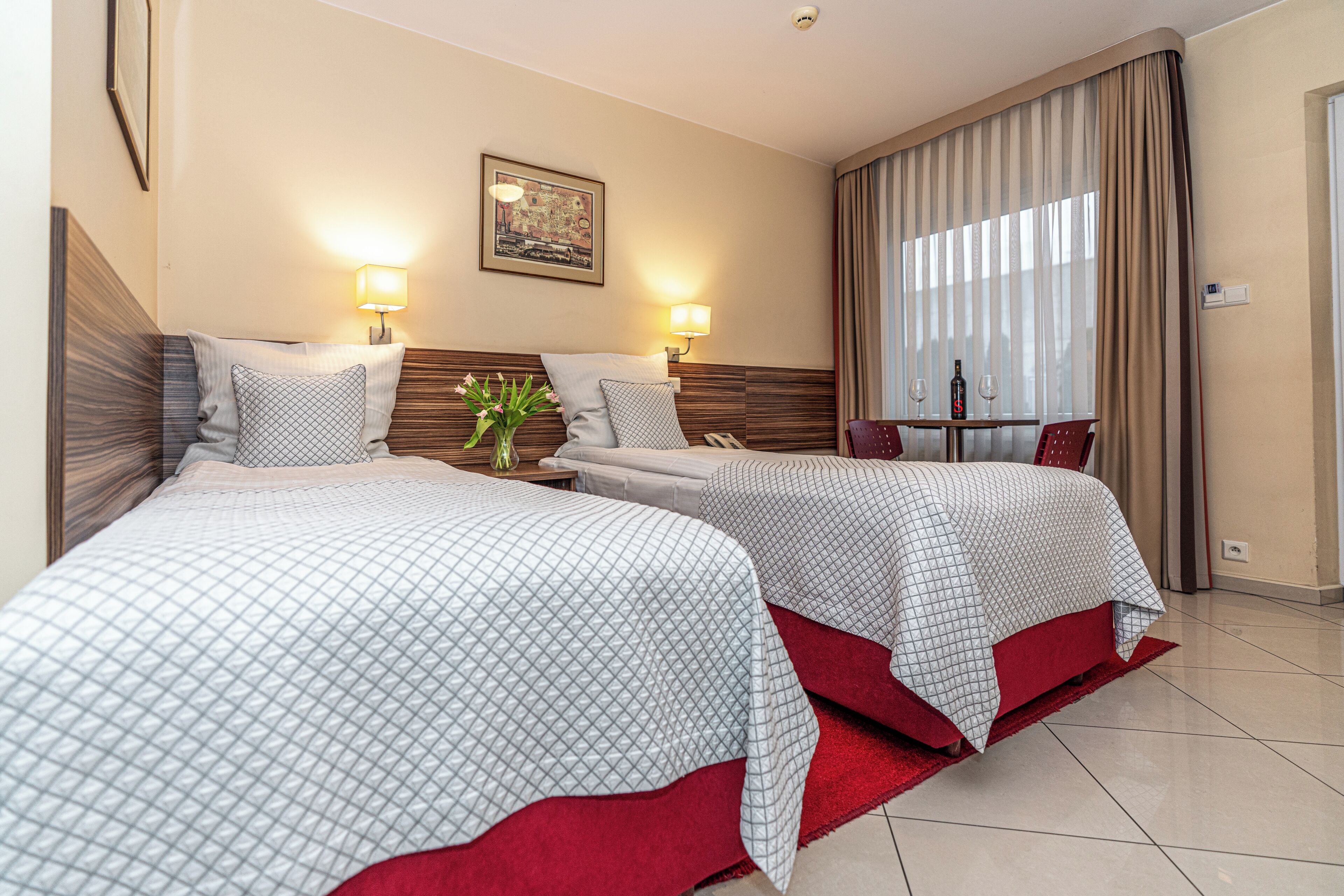 A hotel room with two beds, a dining table, and a large window with curtains.