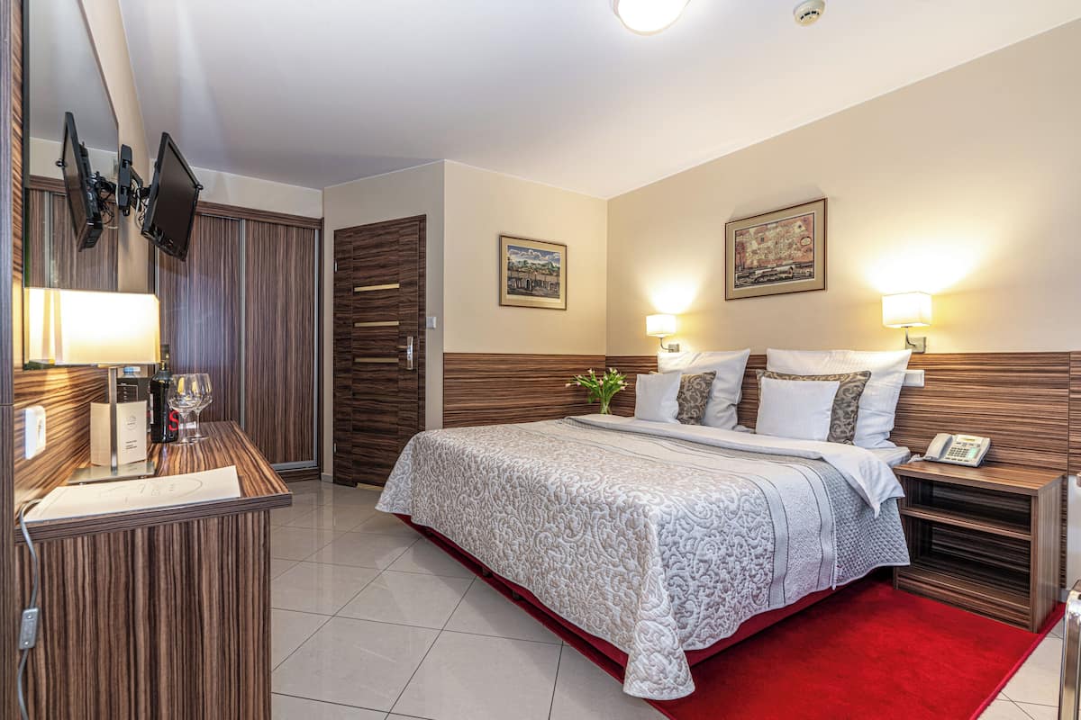 A modern hotel room with a large bed, a desk with a lamp, and a wardrobe.