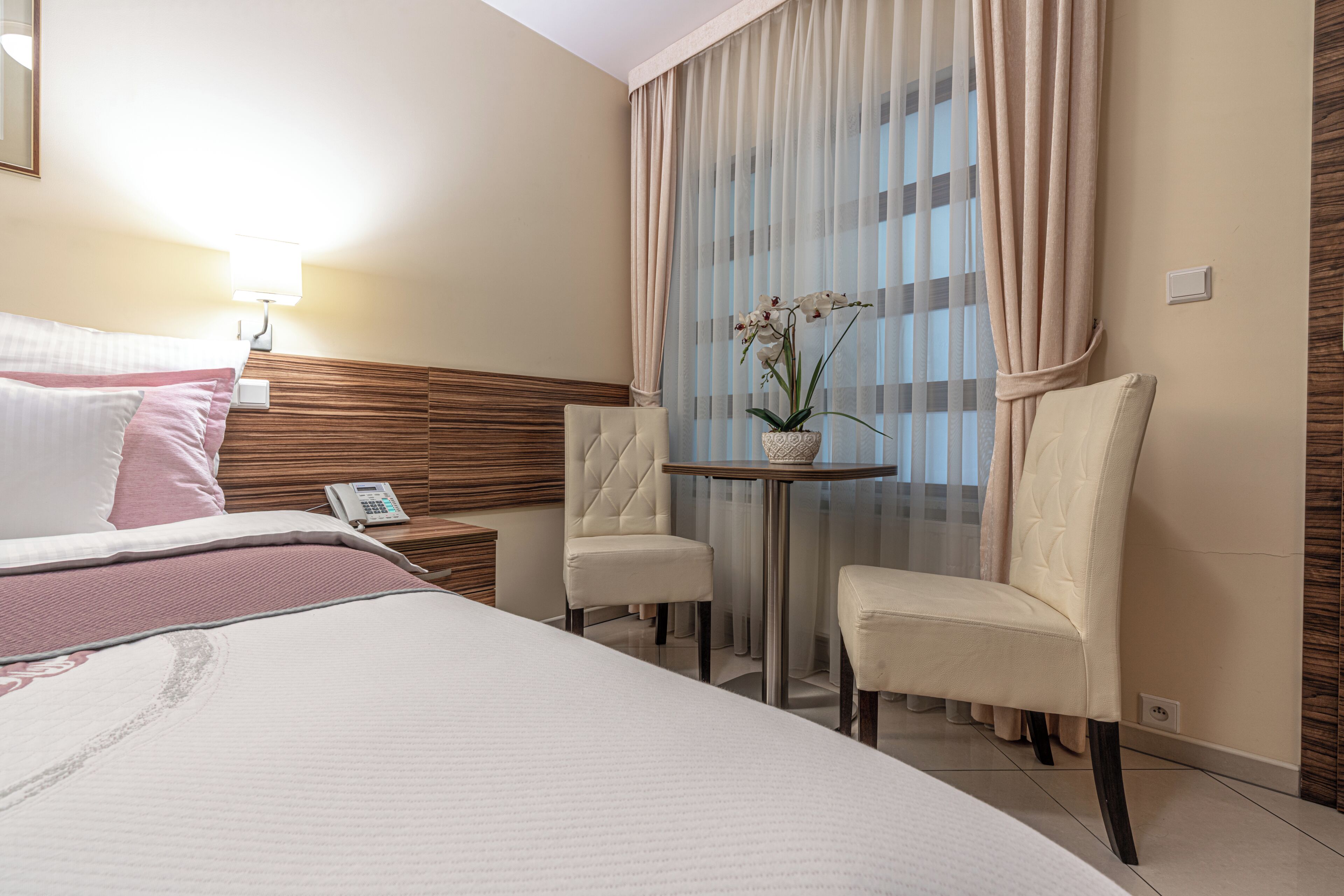 A hotel room with a bed, two chairs, a small table, and a potted plant.
