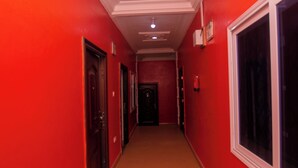 Un couloir aux murs rouges et au sol carrelé, qui mène à une porte au fond.