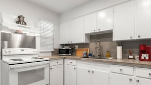 A modern kitchen with white cabinets, a stainless steel range hood, a microwave, and a sink with a faucet. - Bayside Escape | Cozy Hideaway Near Bayshore (Tampa)