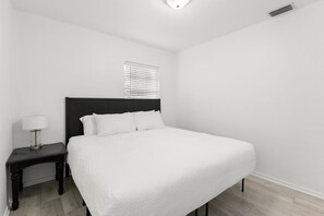 Un dormitorio con una cama grande, una mesita de noche, una lámpara y una ventana con persianas.