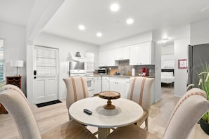 Una cocina moderna con armarios blancos, un comedor con mesa redonda y una sala de estar con sofá.