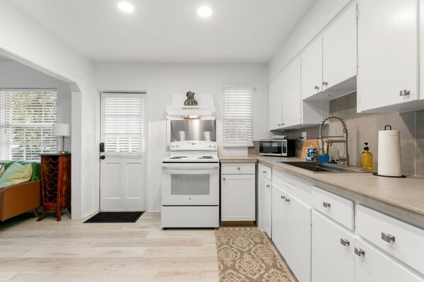 A modern kitchen with white cabinets, a built-in oven, microwave, and sink.