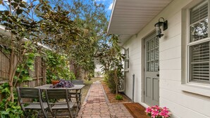 A patio with a table and chairs, a potted plant, and a pathway leading to a house with a door and windows. - Bayside Escape | Cozy Hideaway Near Bayshore (Tampa)