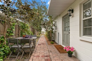 A patio with a table and chairs, a potted plant, and a pathway leading to a house with a door and windows. - Bayside Escape | Cozy Hideaway Near Bayshore (Tampa)