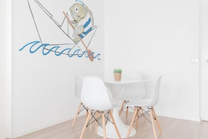 A dining area with a white table and chairs, a wall decal of a fish, and a small plant on the table.