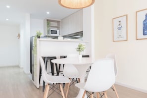 A modern kitchen with white cabinets, a microwave, and a dining area with white chairs and a round table.
