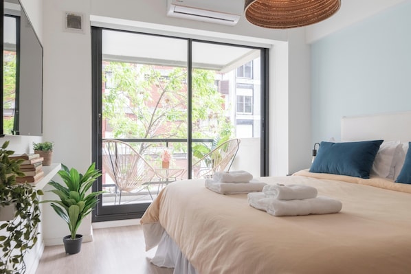 A modern bedroom with a large bed, a balcony with a chair, and a potted plant.