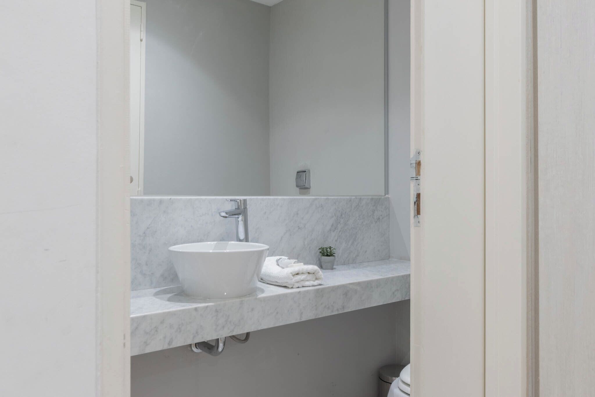 Un baño con un lavabo blanco, un espejo y una pequeña planta en maceta.