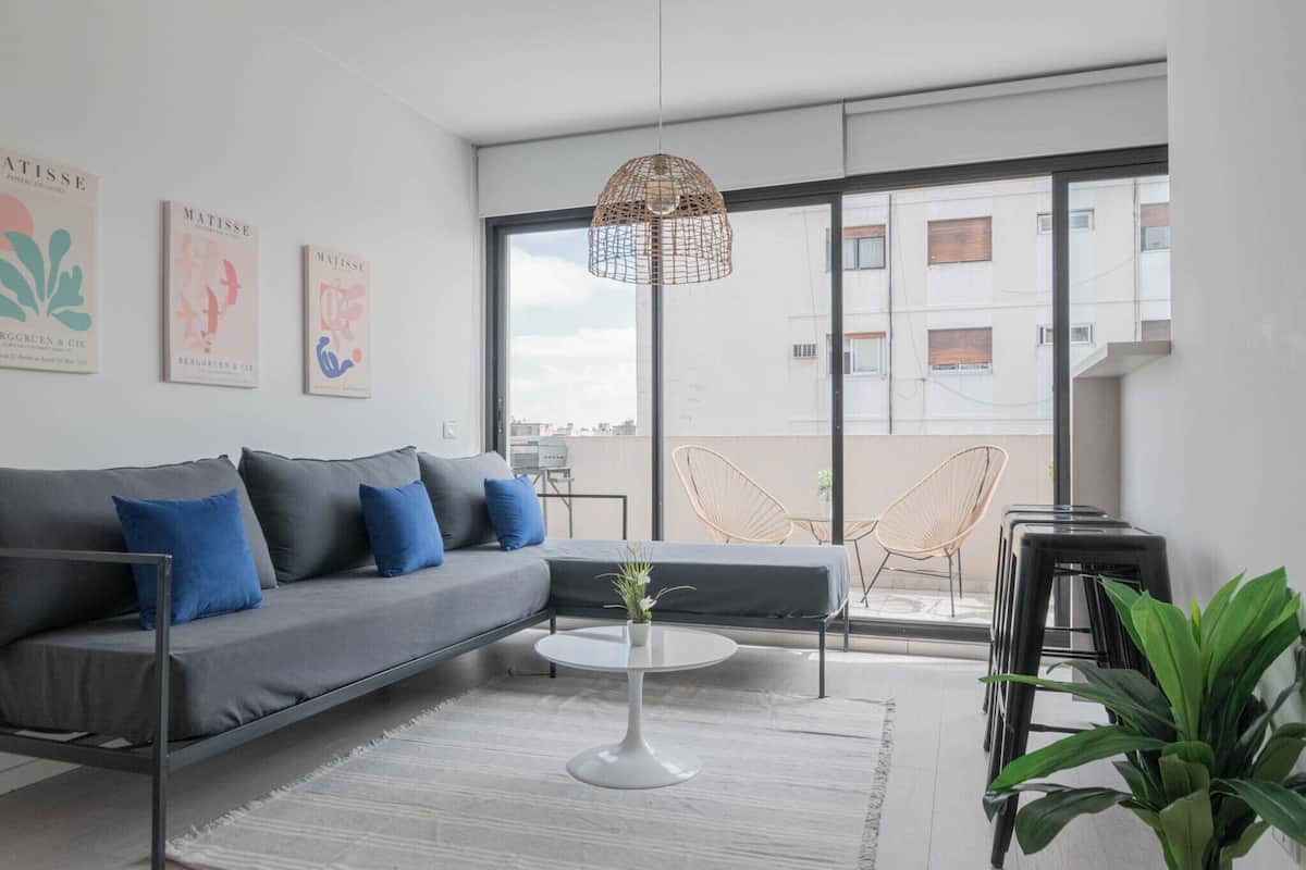 A modern living room with a grey sofa, blue cushions, a white coffee table, and a hanging light fixture.