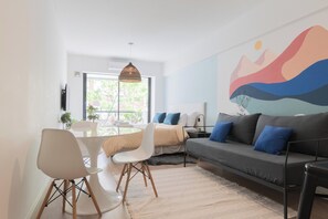 Ein modernes Wohnzimmer mit einer Couch, Sesseln, einem Esstisch und einem großen Fenster.