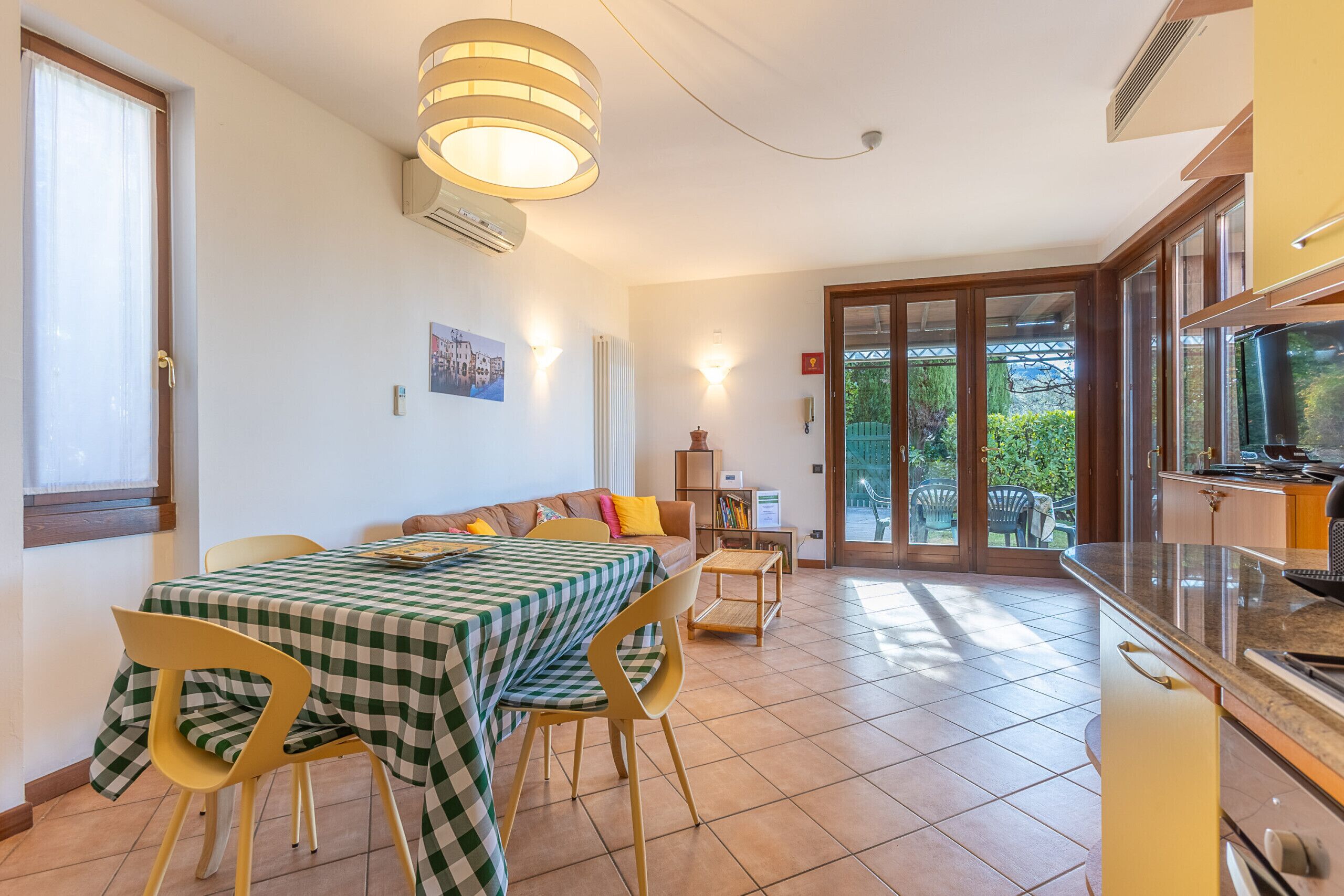 Zona pranzo con tovaglia a quadri, sedie e vista sull'esterno tramite una porta in vetro.