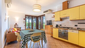 A compact kitchen with yellow cabinets, a Bosch dishwasher, and a dining area with a checkered tablecloth. - Tina Home Lake View (Garda)
