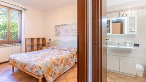 A bedroom with a bed, a window, a painting, and a bathroom with a sink and mirror. - Tina Home Lake View (Garda)