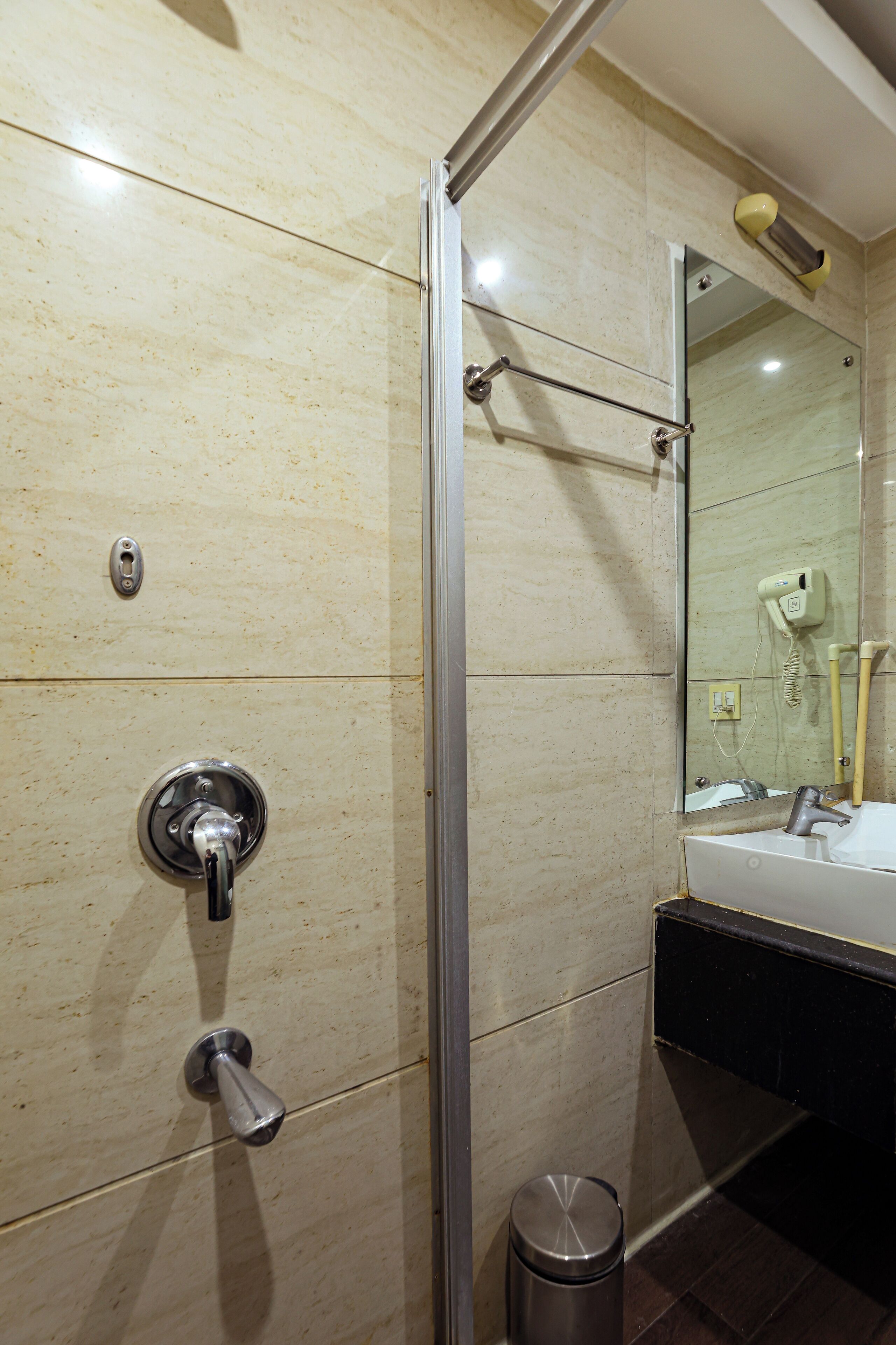 A bathroom with a glass shower door, a sink with a mirror, and a trash can.